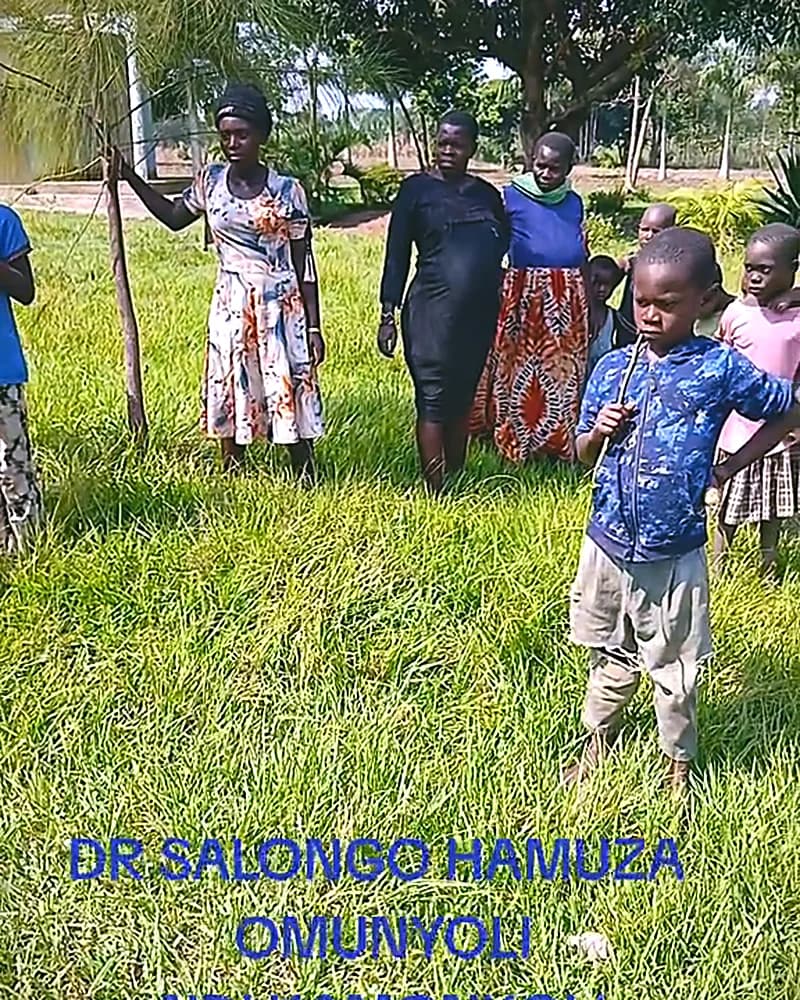 A group walking through green grass towards a village homestead